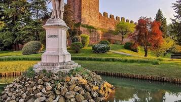 Eine Statue auf einem Steinsockel in einem Park, im Hintergrund ein Schloss.