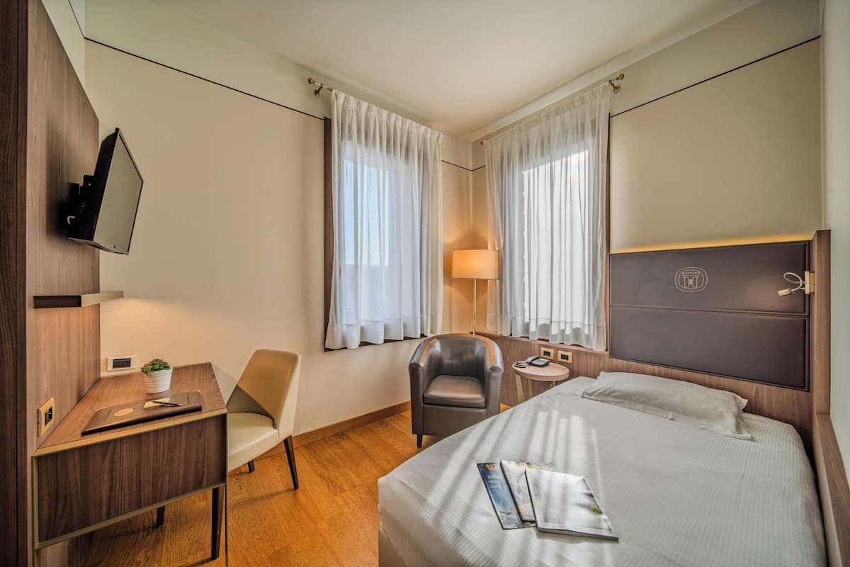 A hotel room with a bed, a desk, a chair, a lamp, and a television.