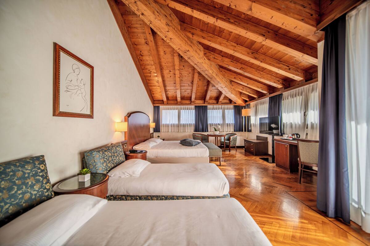 A hotel room with three beds, wooden ceiling beams, a desk, and a television.