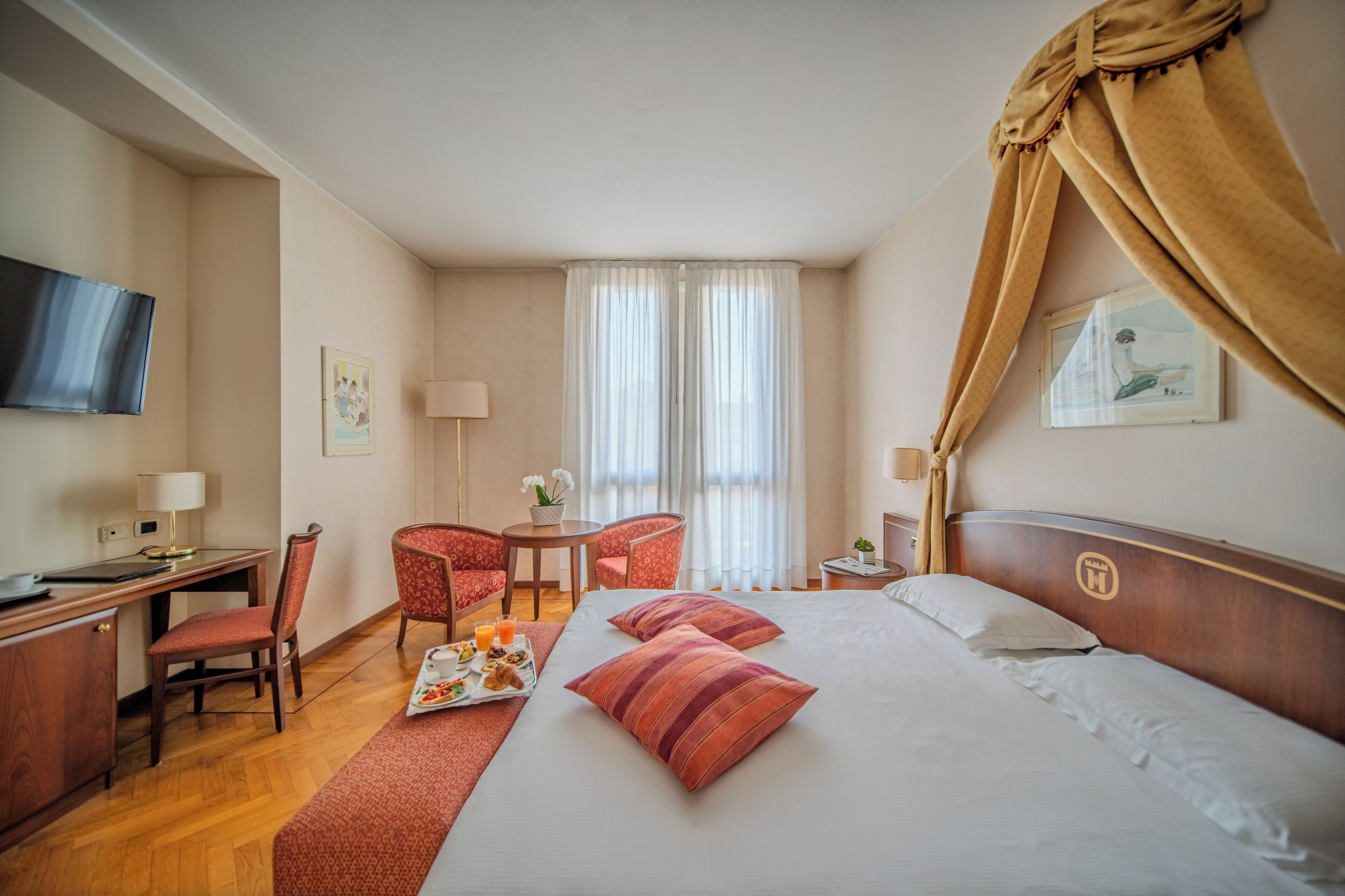 Une chambre d’hôtel avec un lit, un bureau, une chaise, une télévision et une fenêtre avec des rideaux.
