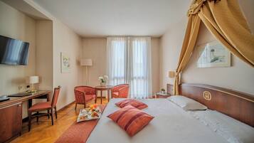Une chambre d’hôtel avec un lit, un bureau, une chaise, une télévision et une fenêtre avec des rideaux.