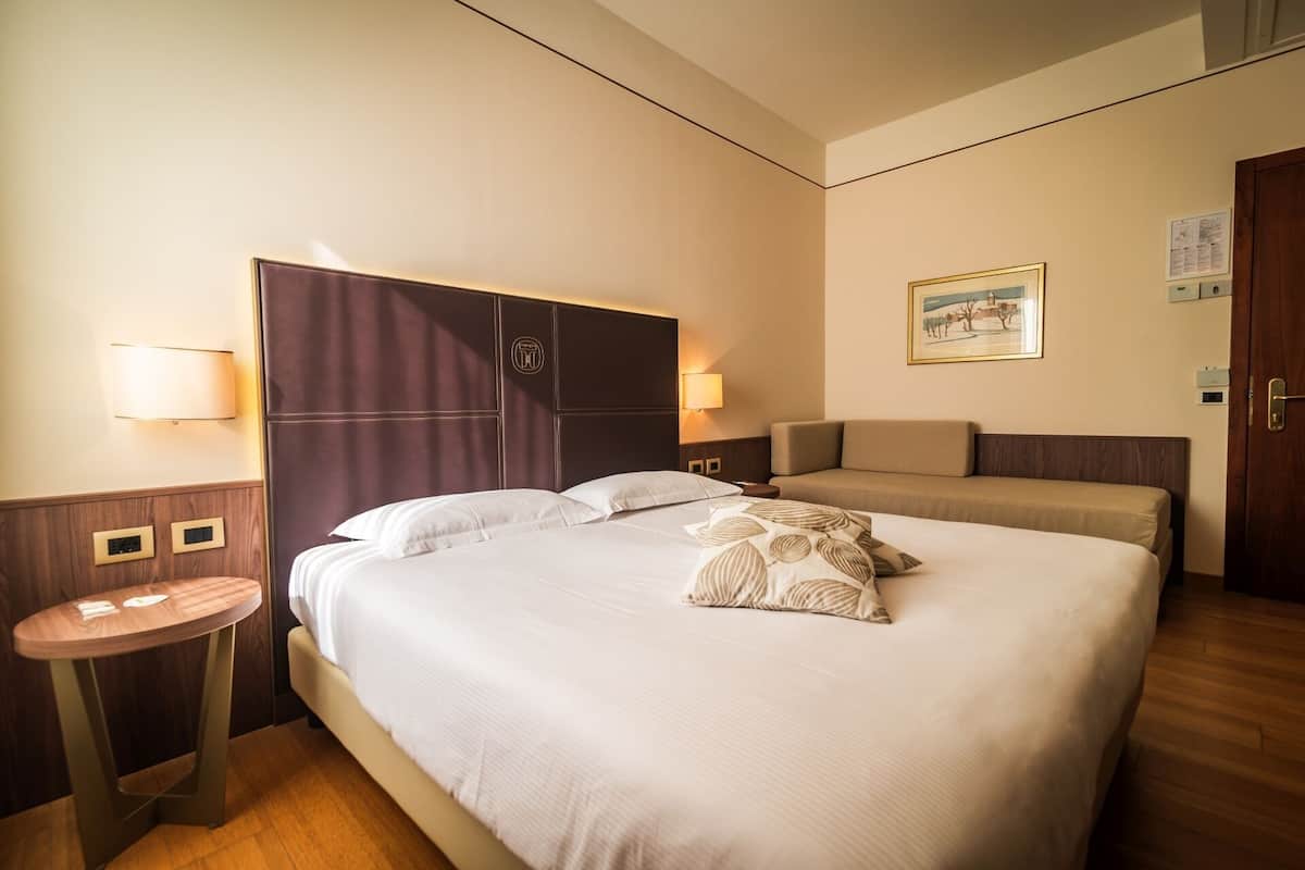 A hotel room with a large bed, a bedside table, a chair, and a small round table.