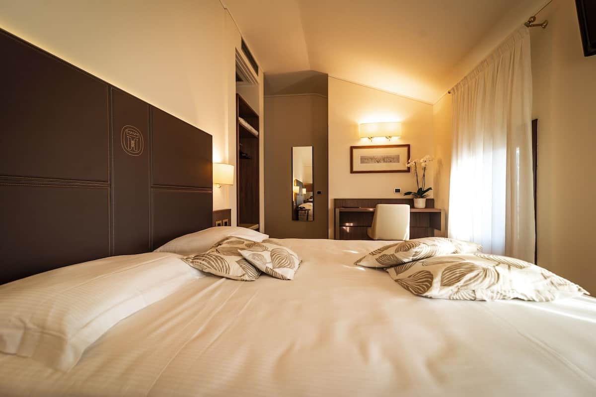 A hotel room with a large bed, a nightstand, a desk, a chair, and a mirror.