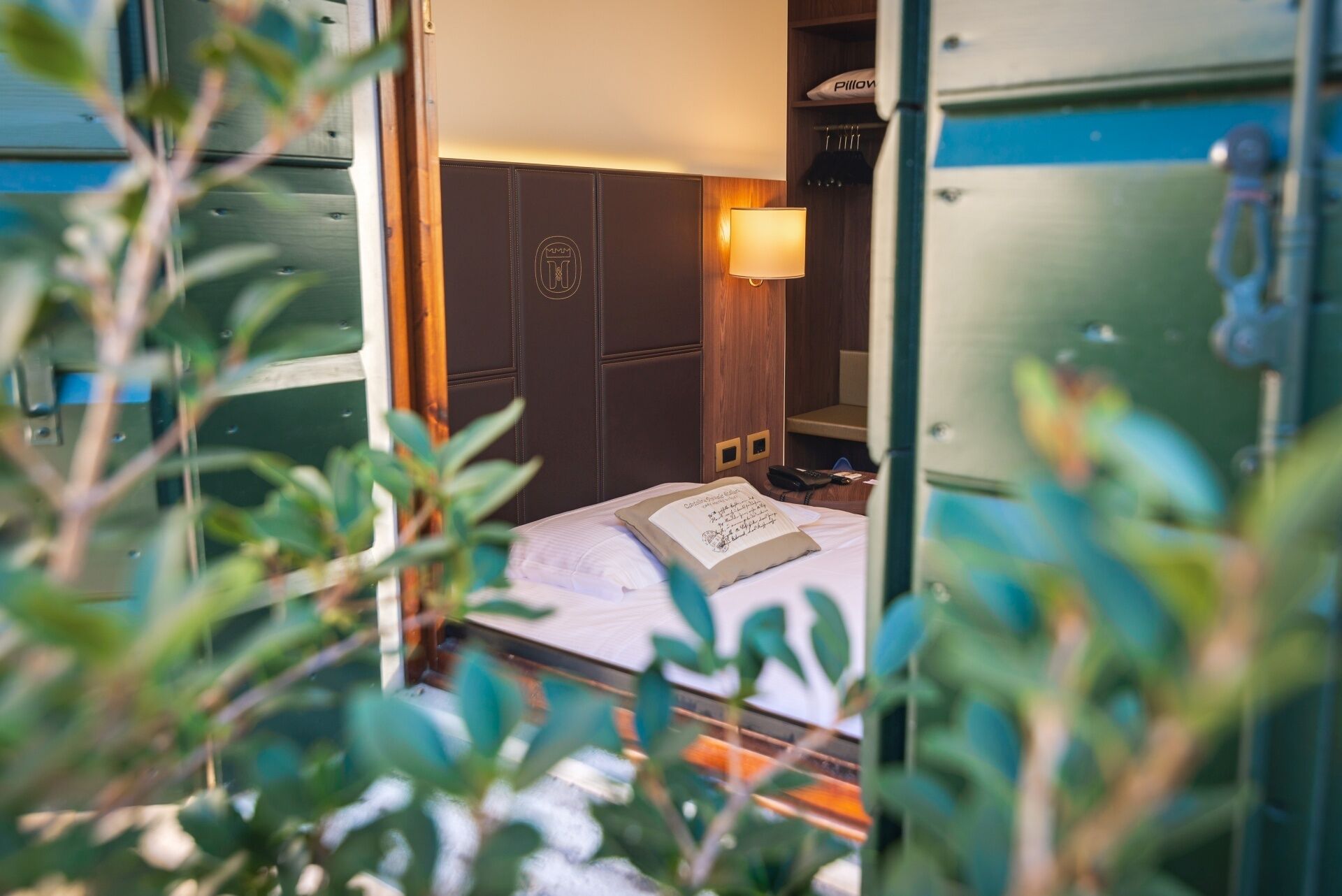 Une chambre d’hôtel de taille réduite, comprenant un lit, une lampe de chevet, une armoire et une petite table avec un téléphone et un livre.