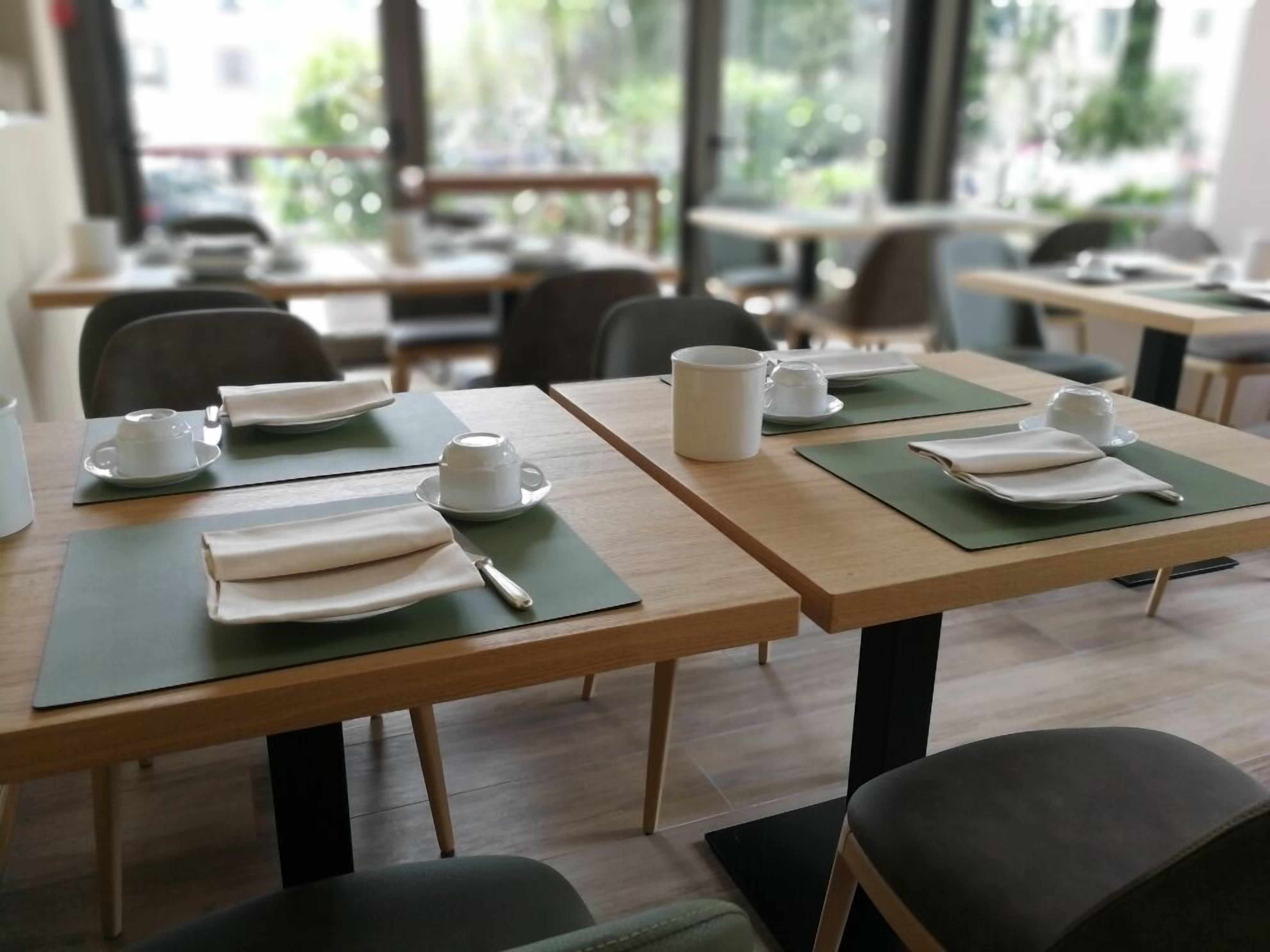 A clean, modern dining area with tables set for two, featuring neatly folded napkins and white cups and saucers.