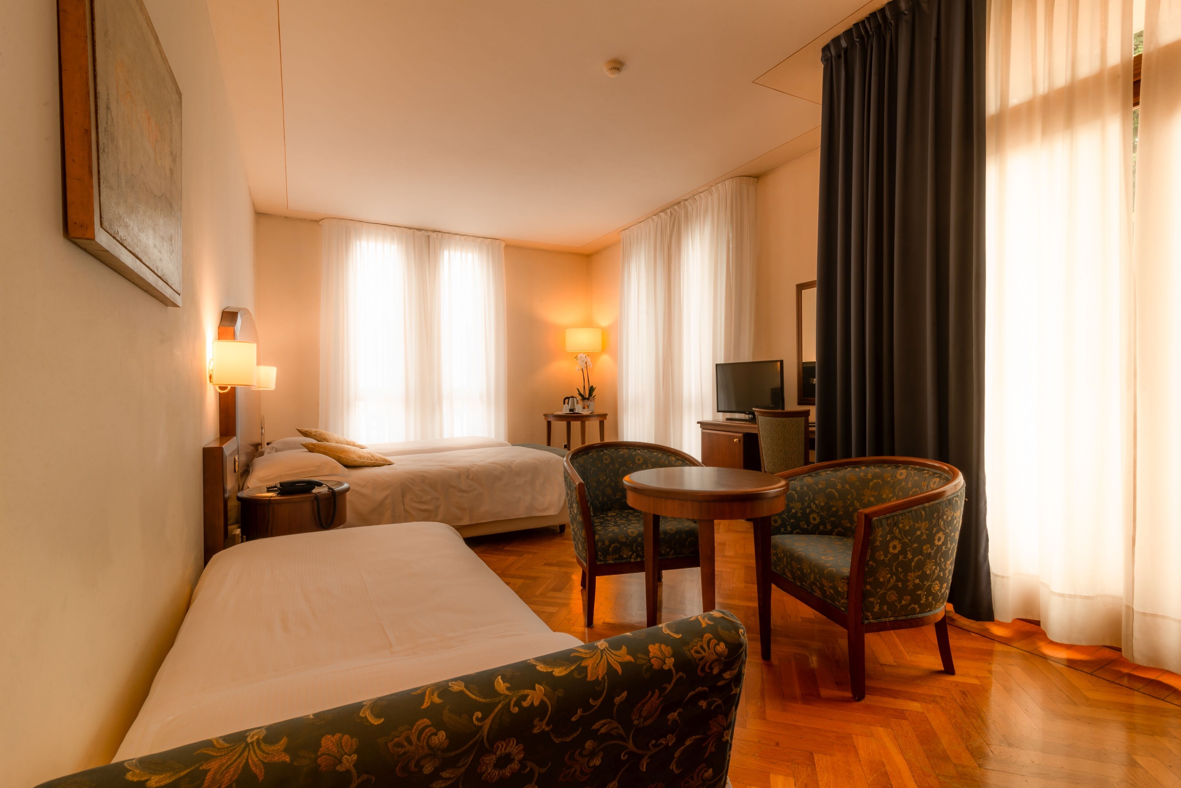 Et hotelværelse med en seng, to stole, et lille bord, et fjernsyn og en lampe.