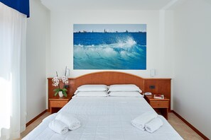 A hotel room with a large bed, white linens, a wooden headboard, a nightstand with a phone and a book, and a wall-mounted painting of a wave. - Hotel Croce di Malta (Imperia)