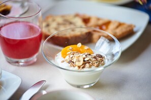 A glass of red juice, a bowl of yogurt with granola and orange, and a plate with bread slices. - Hotel Croce di Malta (Imperia)