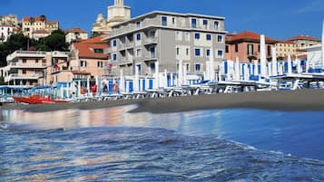 Un edificio costero con varios balcones, una playa al frente y un cielo azul despejado.