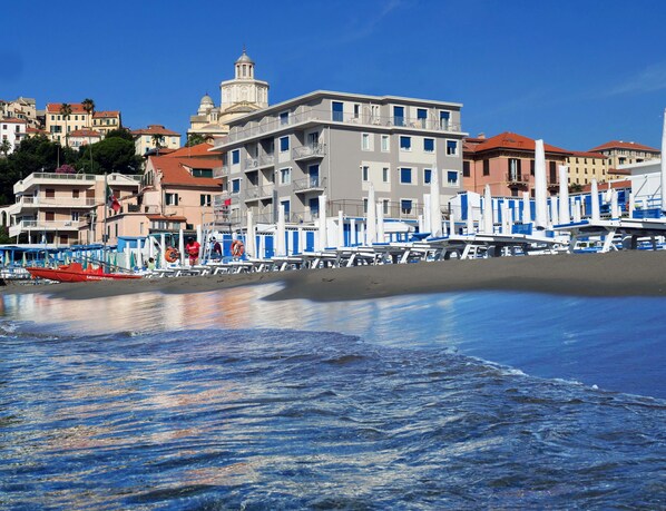 A coastal building with multiple balconies, a beach in the foreground, and a clear blue sky. - Hotel Croce di Malta (Imperia)
