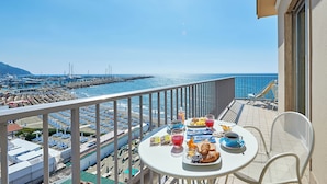 Un balcon avec une table dressée pour le petit-déjeuner, donnant sur une plage et une jetée.