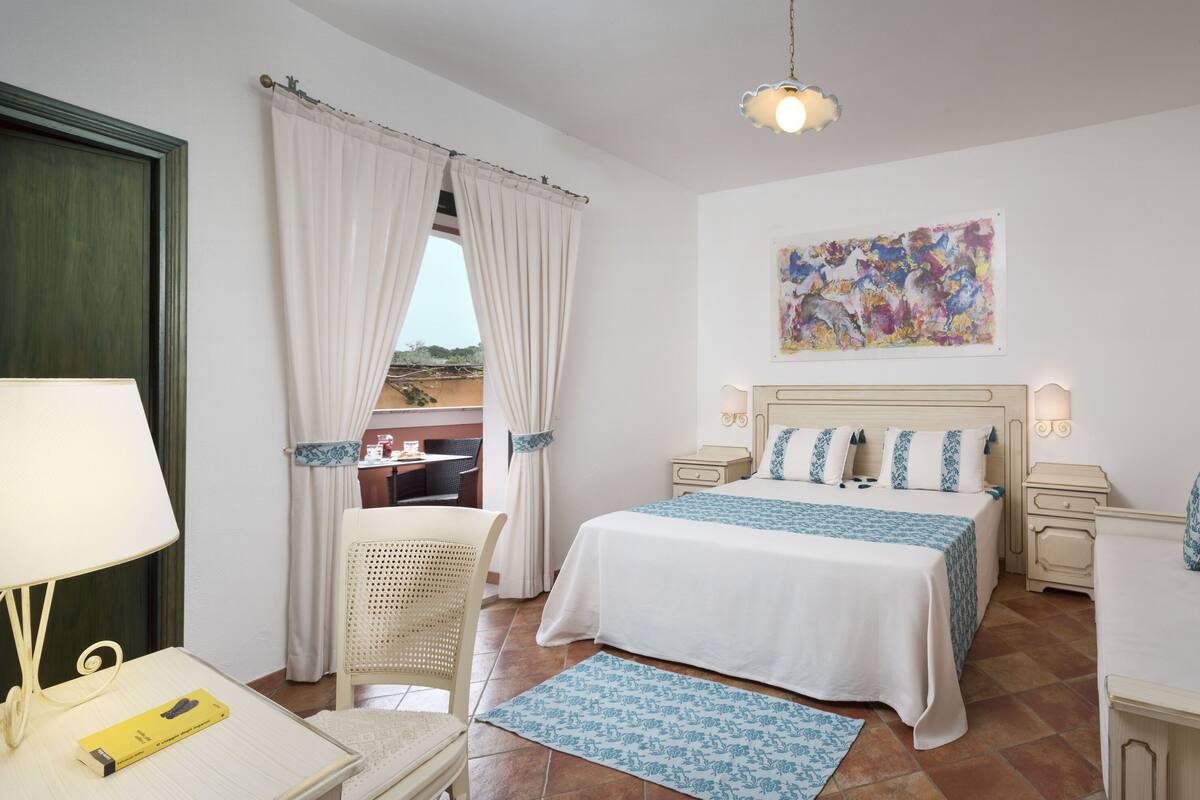 A bedroom with a bed, bedside tables, a chair, a lamp, and a painting on the wall.