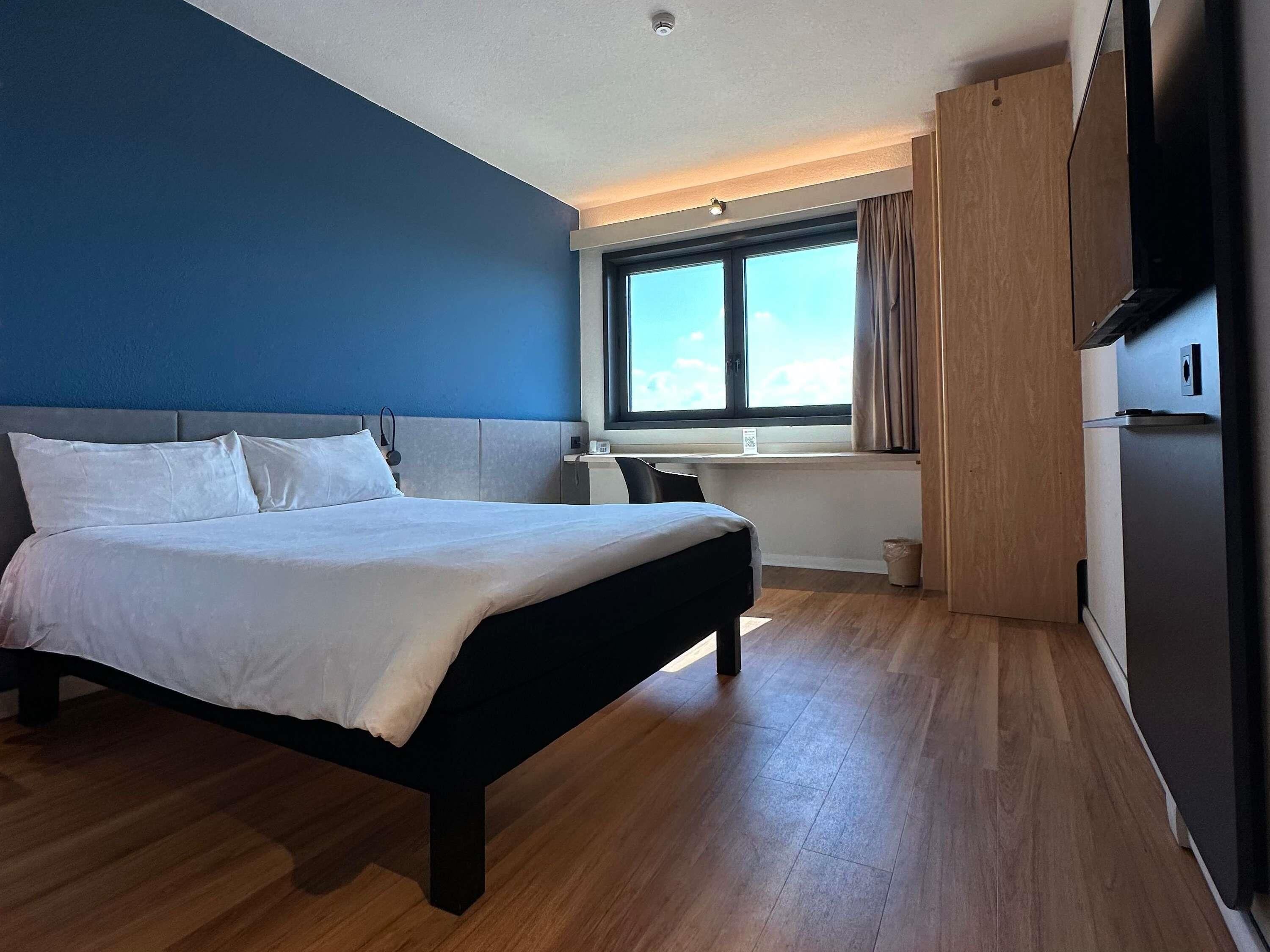 Une chambre d’hôtel moderne, dotée d’un grand lit, d’un bureau et d’une fenêtre avec des rideaux.