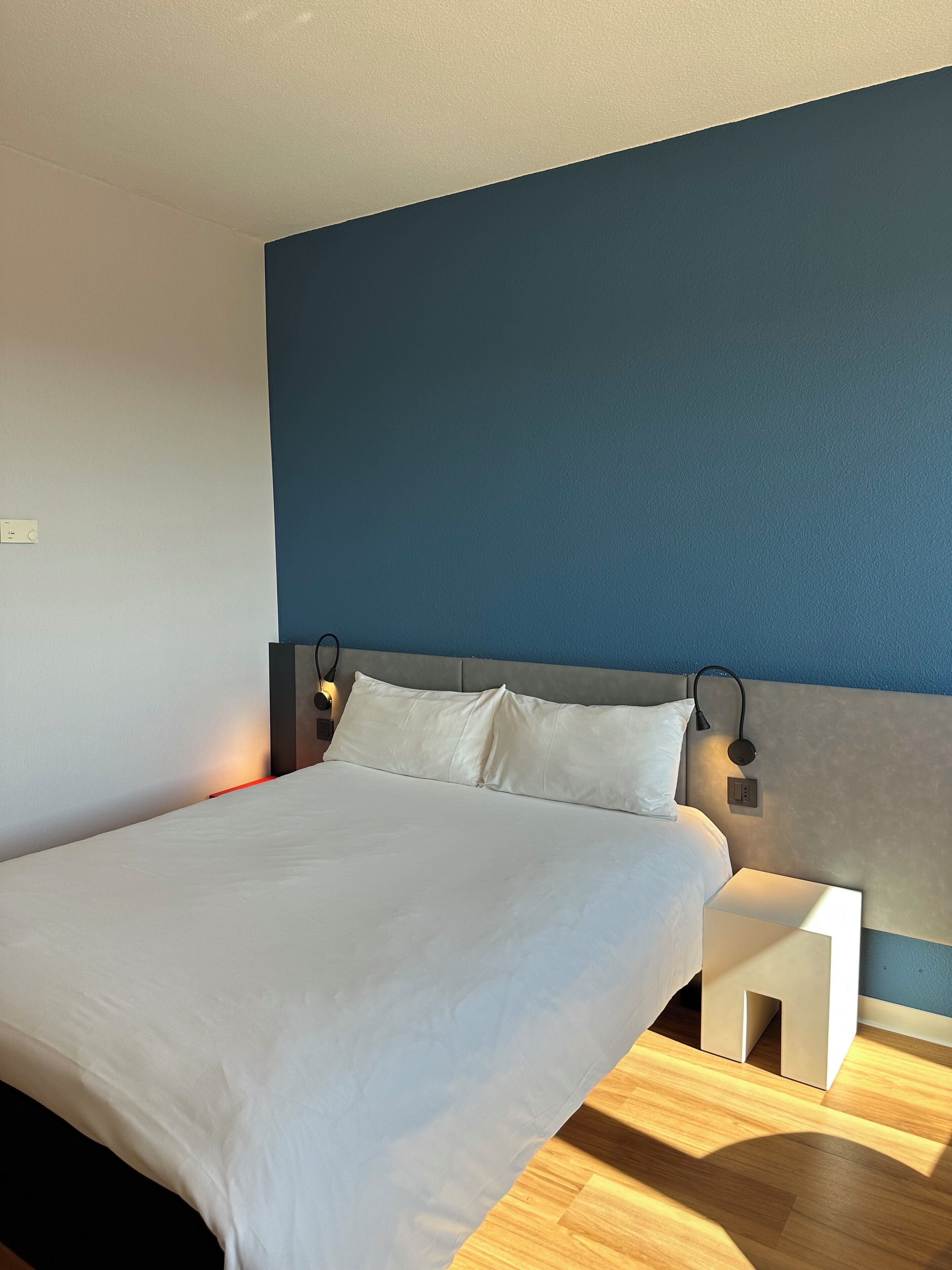 Una habitación de hotel moderna con una cama grande, una mesita de noche y una lámpara de pared.