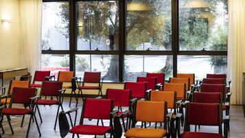 A conference room with rows of chairs, large windows with a view of trees and a parking lot, and a table with a board.