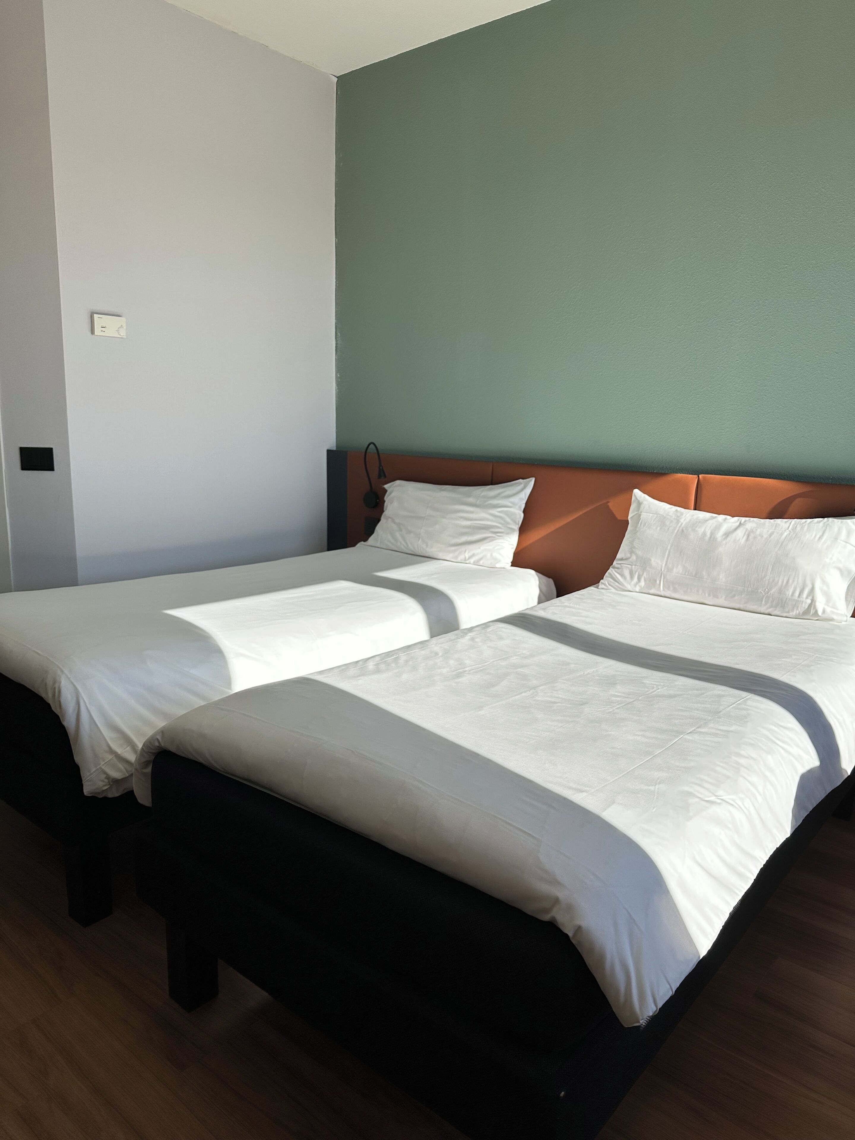 A hotel room with two single beds, a wooden floor, and a green accent wall.