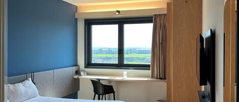A hotel room with a bed, desk, chair, TV, and a large window with a view.