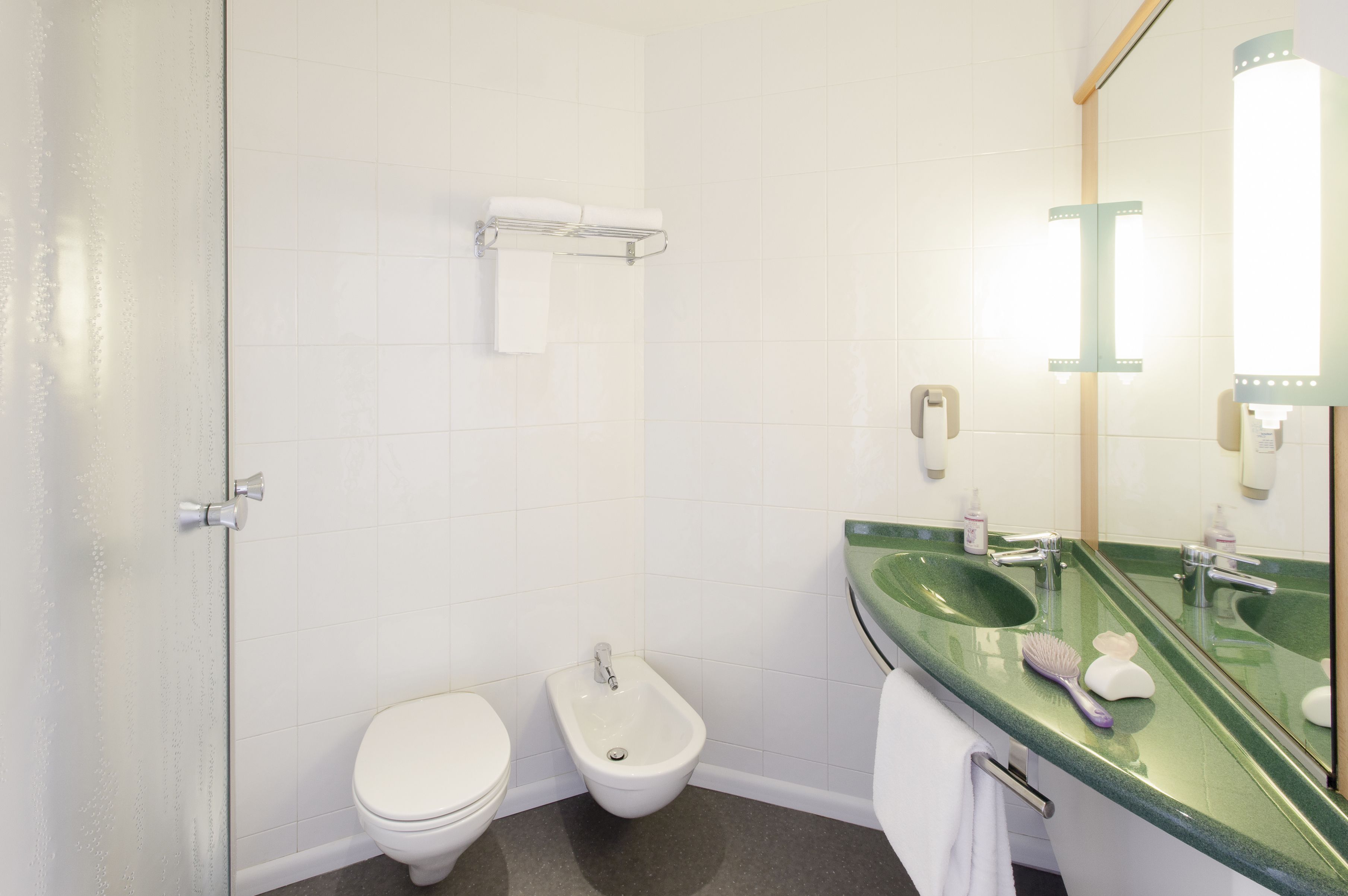 A bathroom with a toilet, bidet, and a green sink with a mirror.