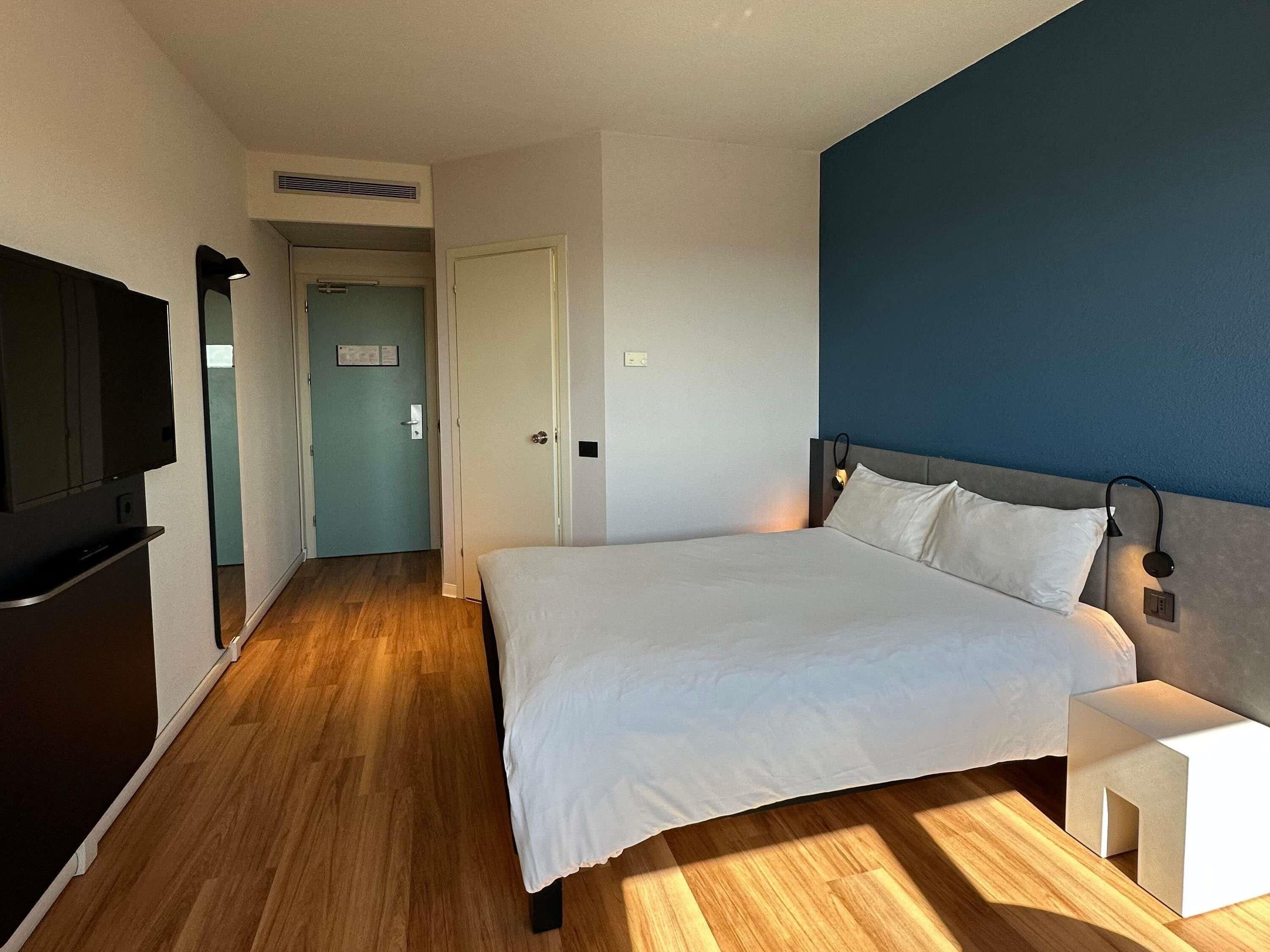 A hotel room with a large bed, a TV, and a wooden floor.