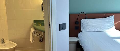 A hotel room with a wooden floor, a white bed, a green sink, and a white toilet.