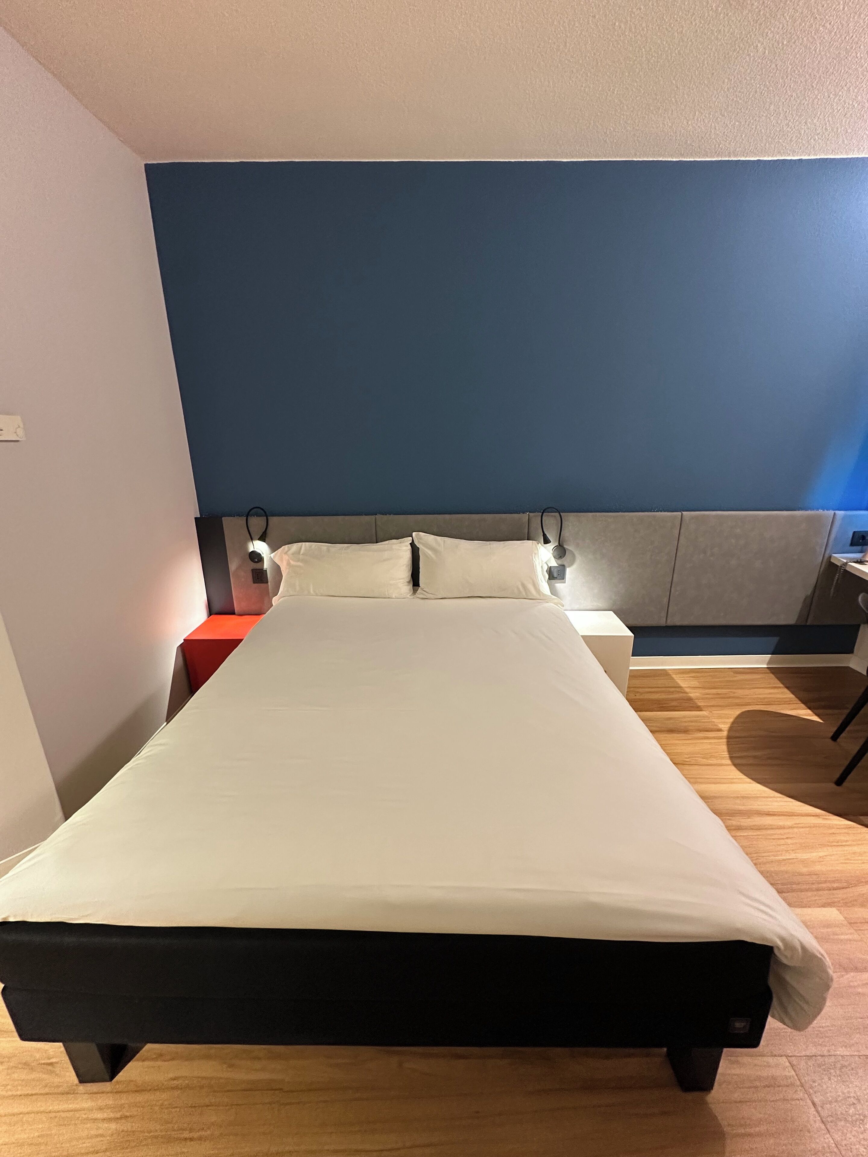 A bed with a white mattress and black frame, a bedside table with a lamp, and a blue wall.