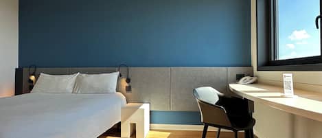 A modern hotel room with a bed, a desk, and a chair.