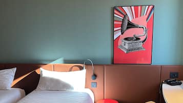 Habitación de hotel con cama, escritorio, silla, taburete rojo y un cuadro colgado en la pared de un fonógrafo.