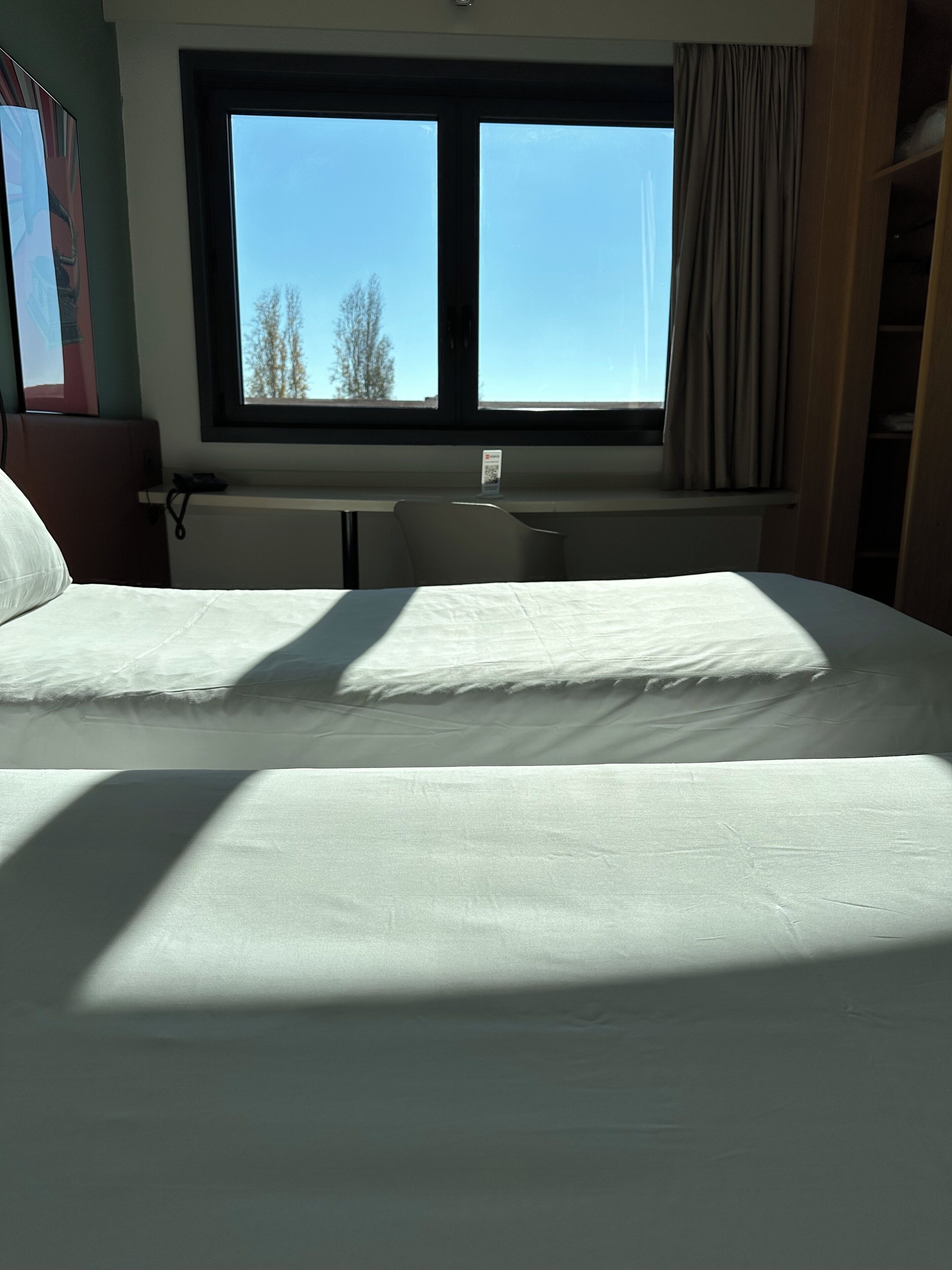 A hotel room with a large bed, a desk, and a window with a view of trees.