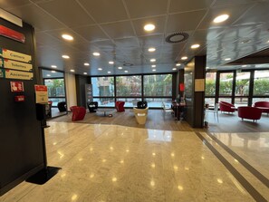 A spacious lobby with a marble floor, modern seating, and large windows offering a view of the outdoors.