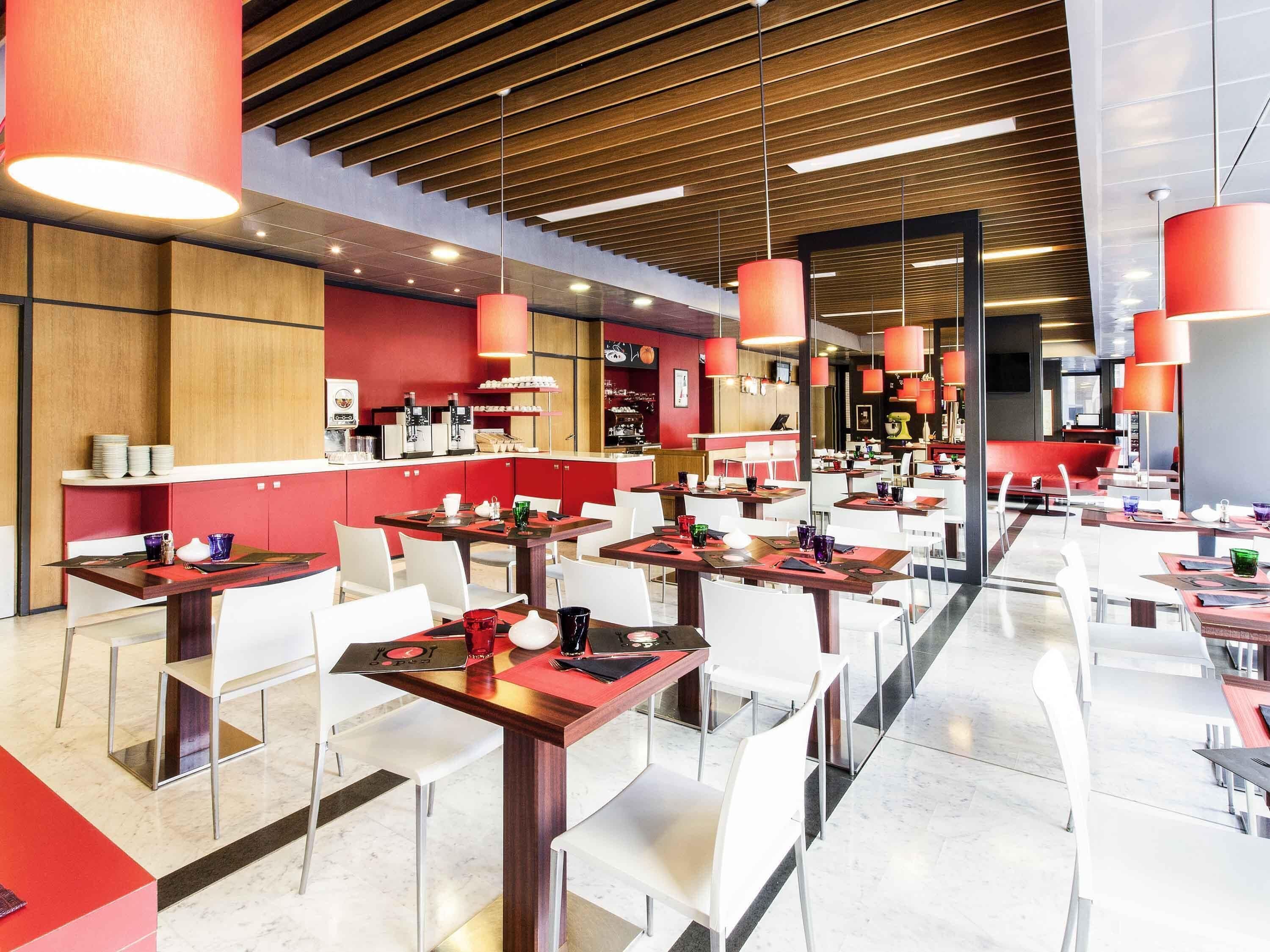 Un restaurante moderno con varias mesas, sillas rojas y blancas, y un techo de madera.