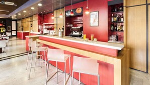 A modern bar area with a red counter, white bar stools, and a variety of bottles and glasses.