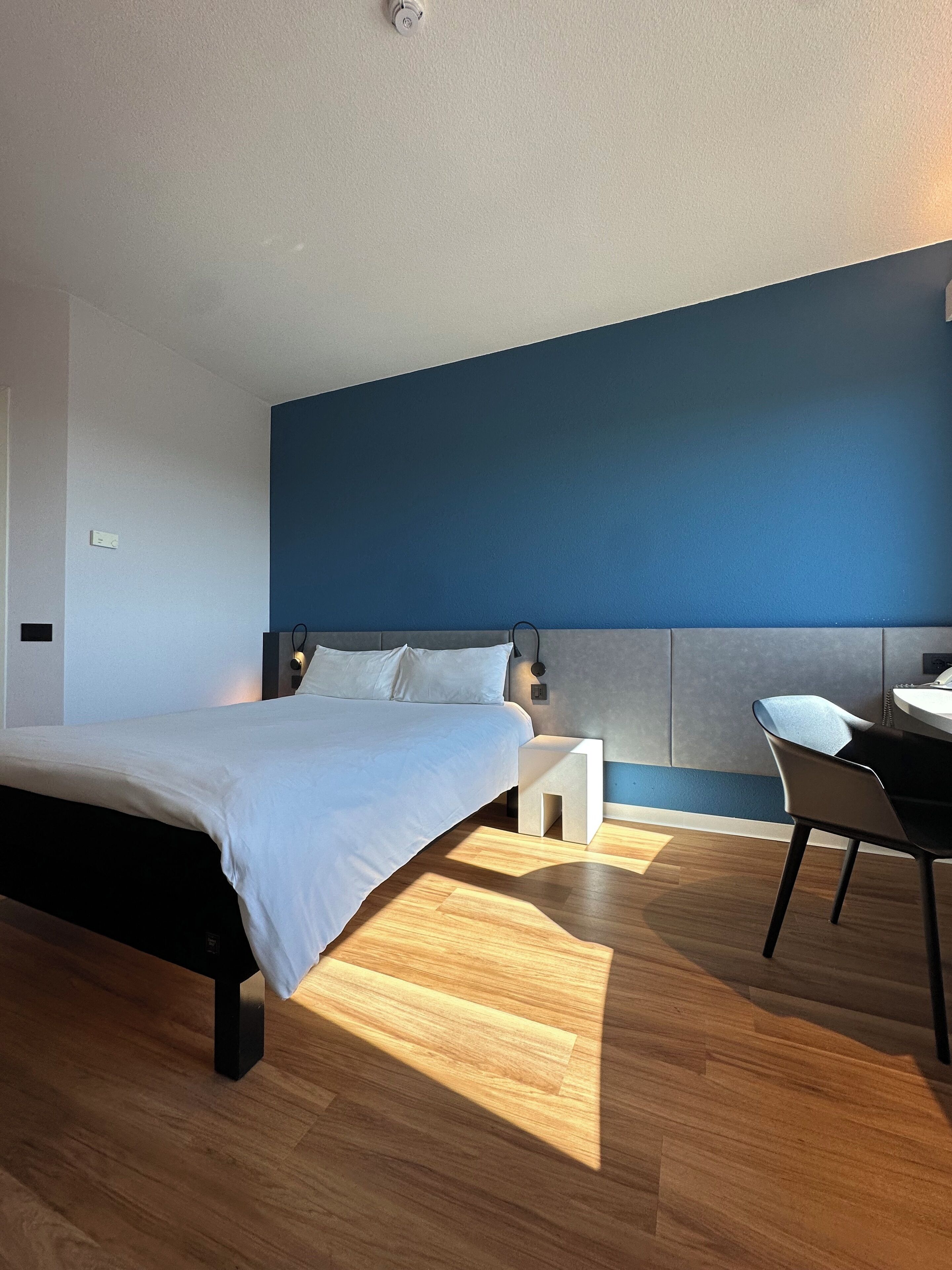 A modern bedroom with a bed, bedside table, and a desk with a chair.