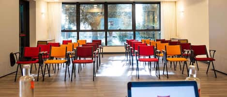 A conference room with rows of chairs, a laptop on a table, and a window with a view of trees.