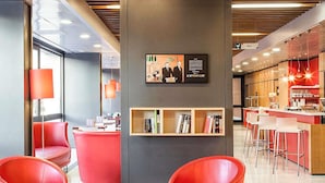 A modern hotel lobby with red chairs, a bar area, and a bookshelf with books.