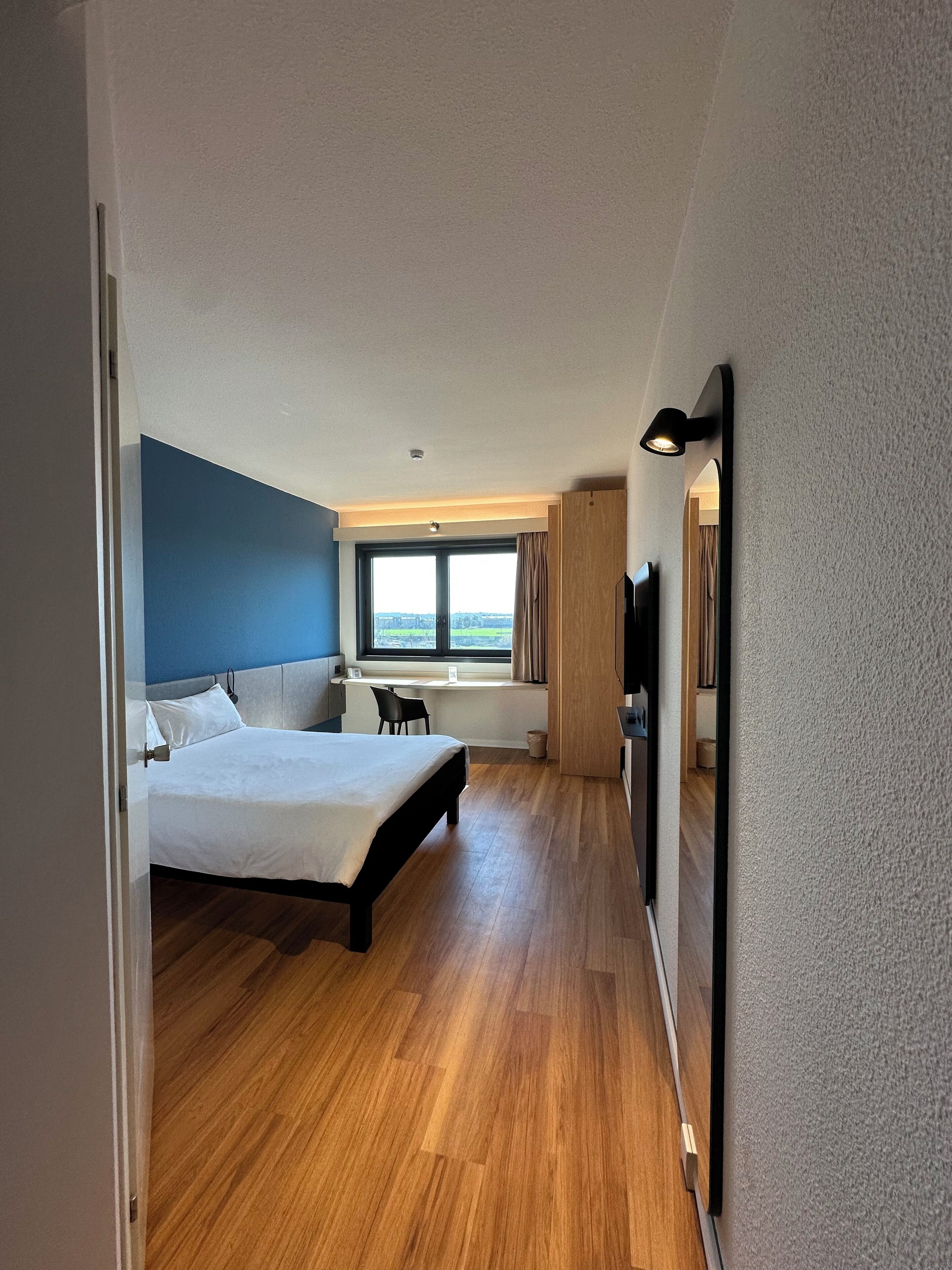 Moderni hotellihuone, jossa on suuri sänky, työpöytä ja televisio.