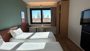 Hotellihuone, jossa on kaksi sänkyä, työpöytä, tuoli, televisio ja ikkuna, jossa on verhot.