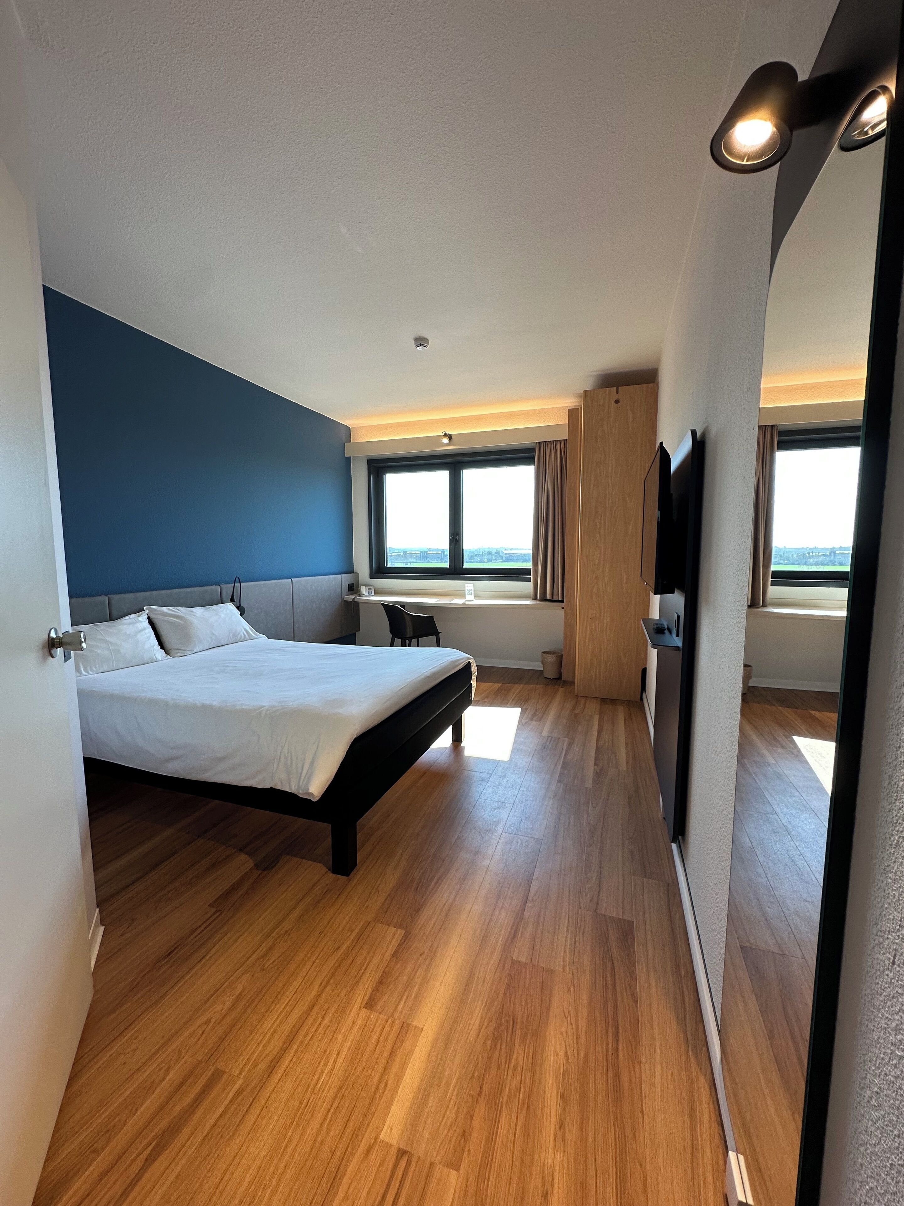 A modern hotel room with a large bed, a desk, a chair, and a TV.