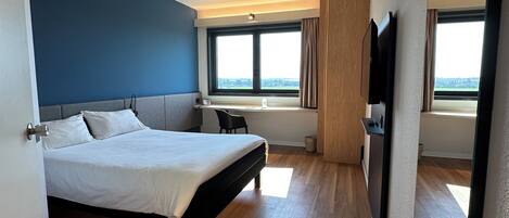 A modern hotel room with a large bed, a desk, a chair, and a TV.