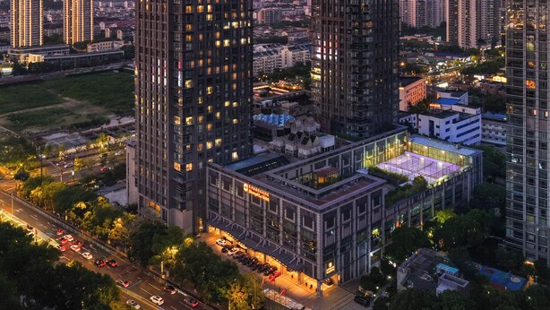 Um edifício alto com design arquitetônico moderno, rodeado por outros edifícios altos e uma rua urbana movimentada.