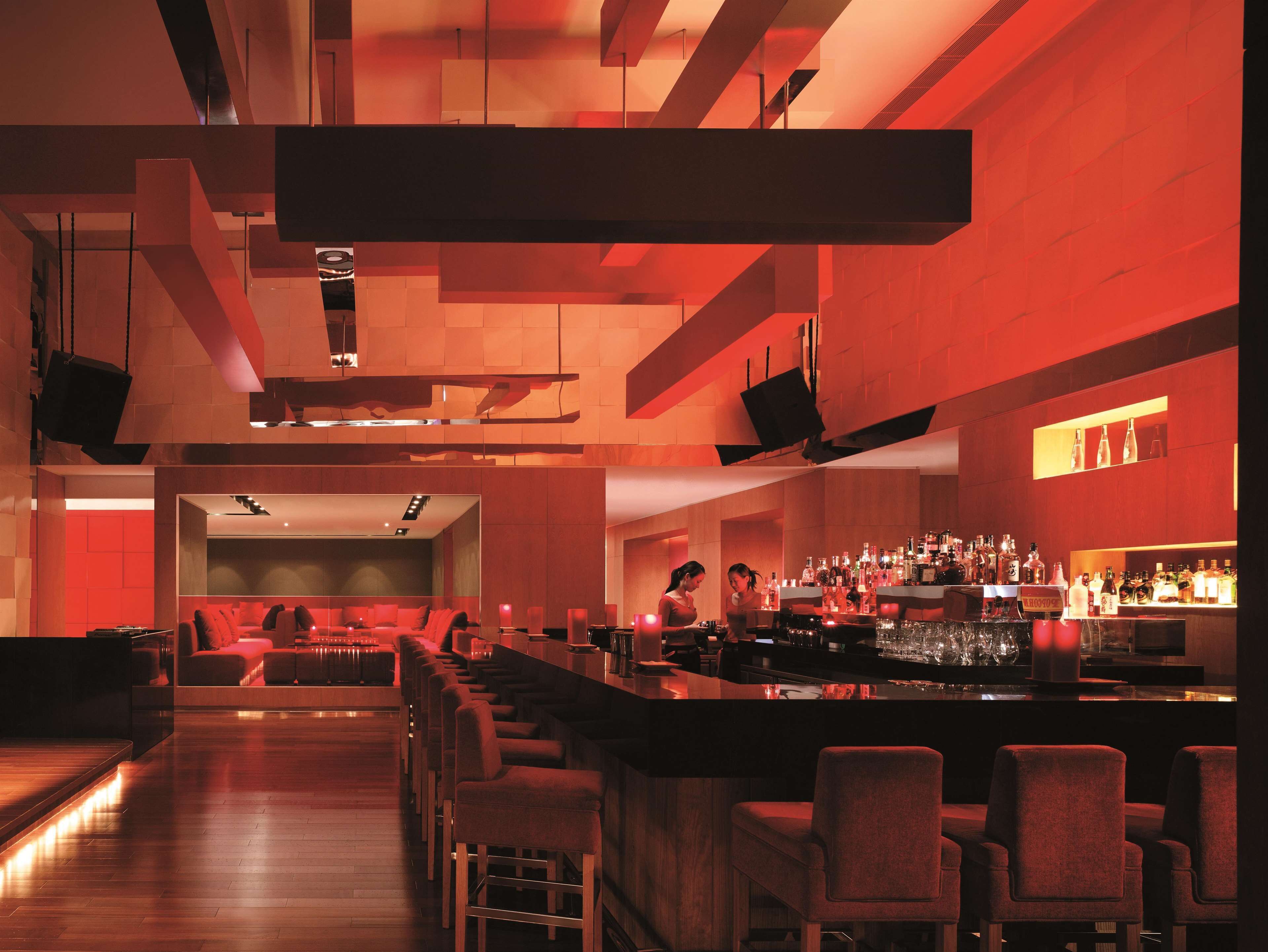 A modern bar with a long counter, multiple bar stools, and a seating area with sofas.