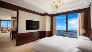 Quarto de hotel com uma cama grande, televisão na parede e vista para a cidade pela janela.