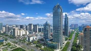 Un edificio de gran altura con fachada de vidrio moderna, rodeado de otros edificios altos y una calle concurrida con coches y zonas verdes.