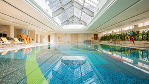 Uma piscina interior com teto de vidro, espreguiçadeiras e um toboágua.