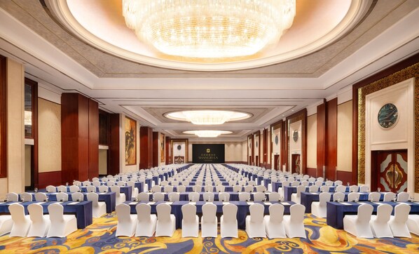 Un salón de conferencias con filas de mesas y sillas, una araña de cristal y un cartel que dice 'SHANGRI-LA SUZHOU'.