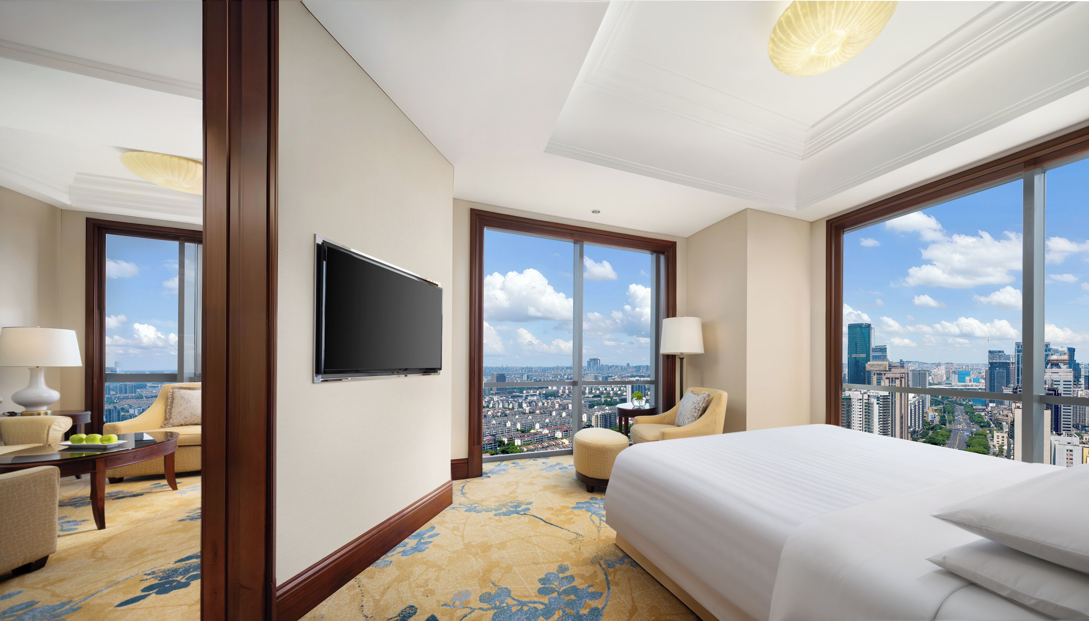 Une chambre d’hôtel avec un grand lit, deux fauteuils, une télévision et une vue sur la ville.