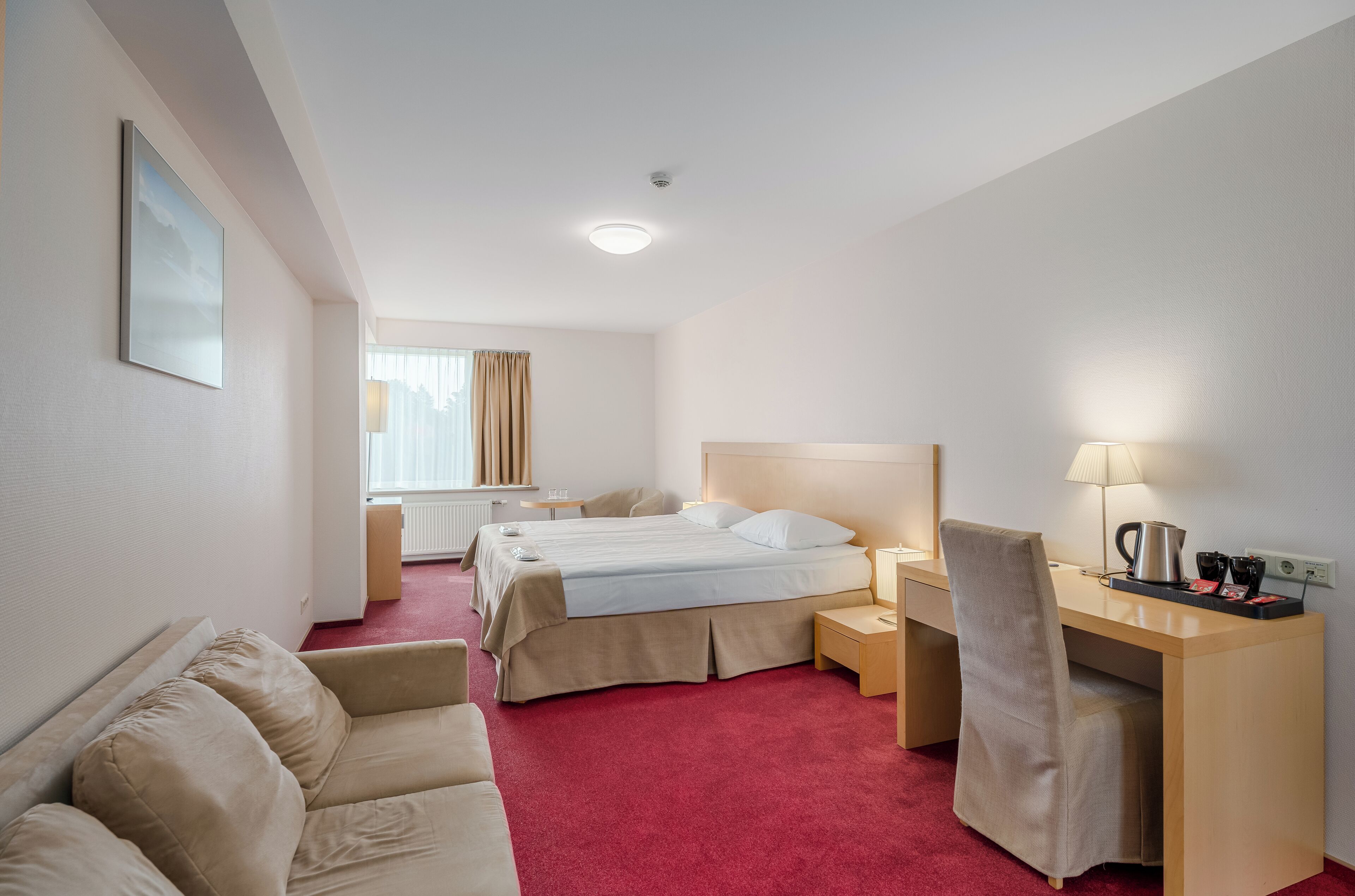 A hotel room with a bed, a desk, a chair, a sofa, and a window with curtains.