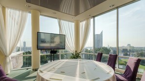 A conference room with a round table, purple chairs, a flat-screen TV, and a city view. - Riga Islande Hotel with FREE parking (Riga)