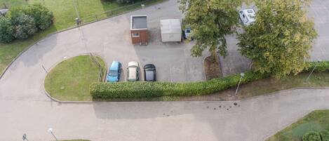 An aerial view of a parking area with several cars, a small building, and a large tree.