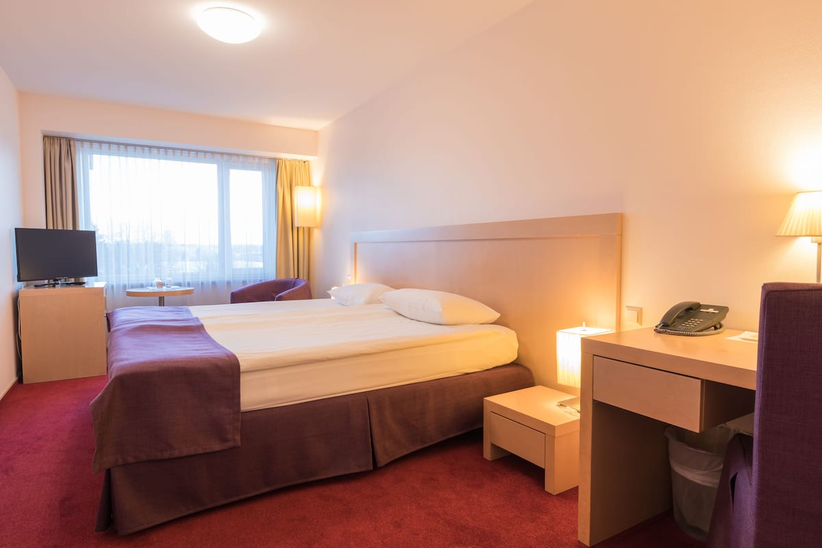 A hotel room with a bed, a desk, a chair, a television, and a window with curtains.