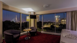 A hotel room with a large window offering a city view, a bed, a chair, and a small table. - Riga Islande Hotel with FREE parking (Riga)